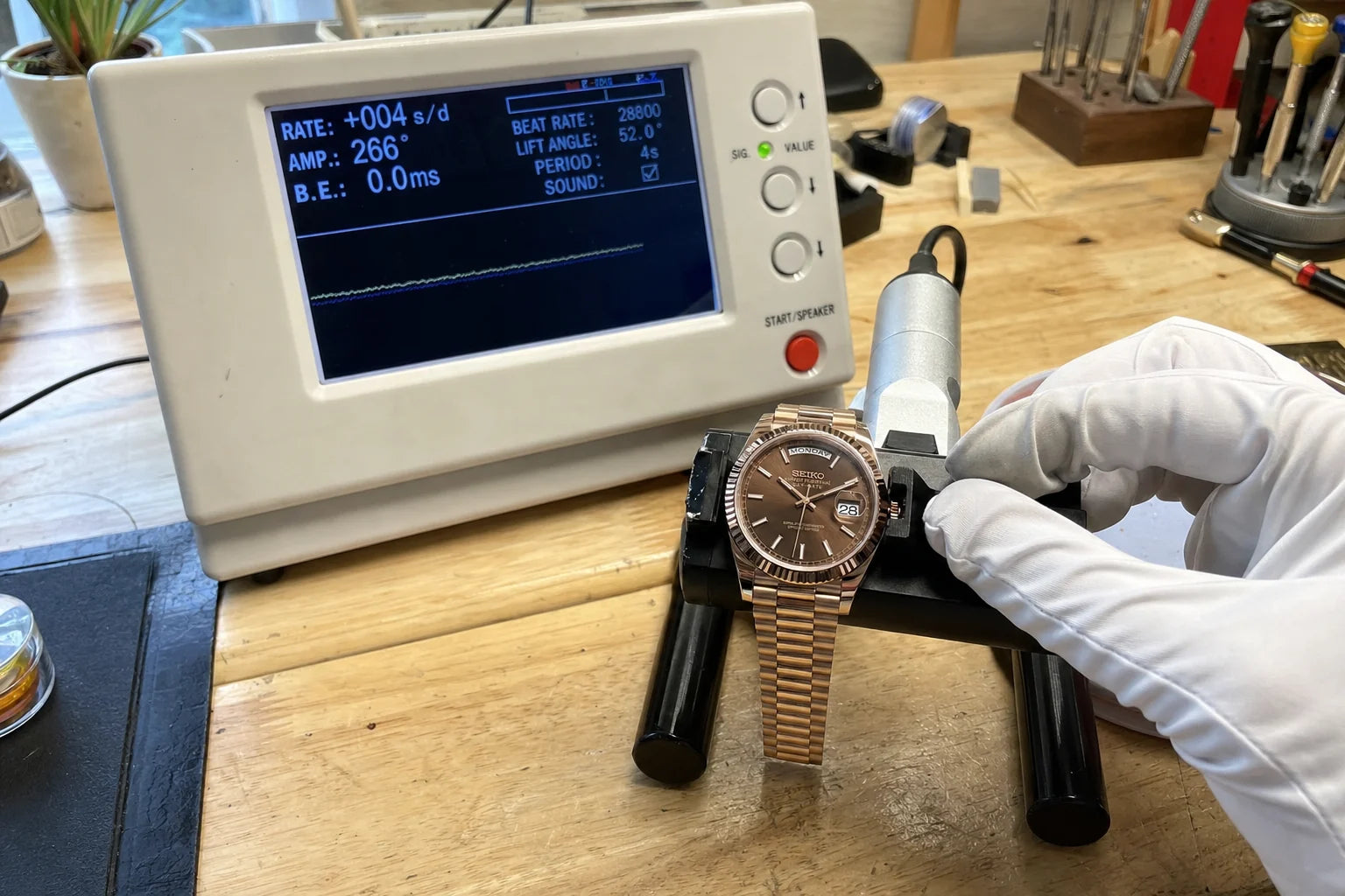 Rose-gold watch undergoing timing inspection on a workbench